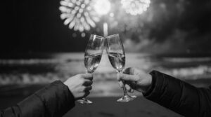Two hands holding champagne flutes and toasting, with fireworks going off in the background